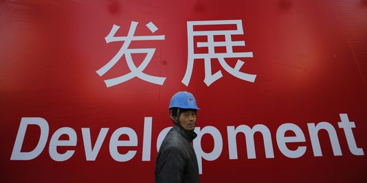 Ouvrier chinois se tenant devant une affiche du développement économique